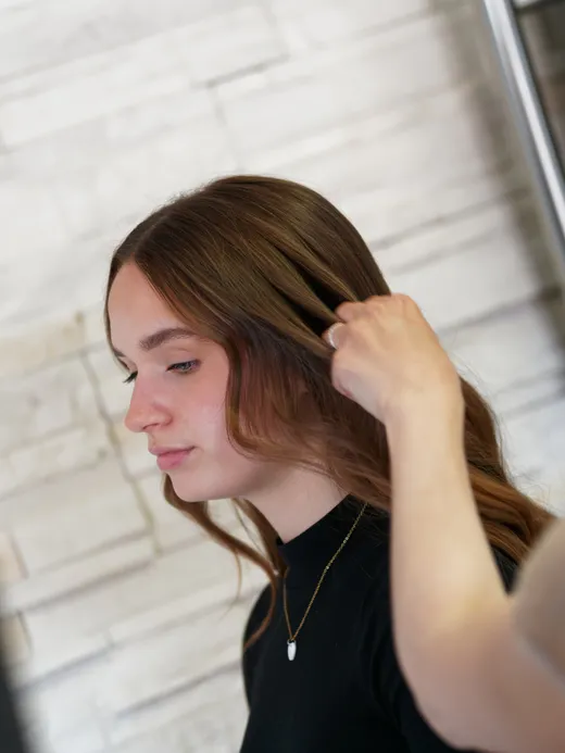 Kundin mit fertig gestylten langen Haaren vor der Steinwand im Salon