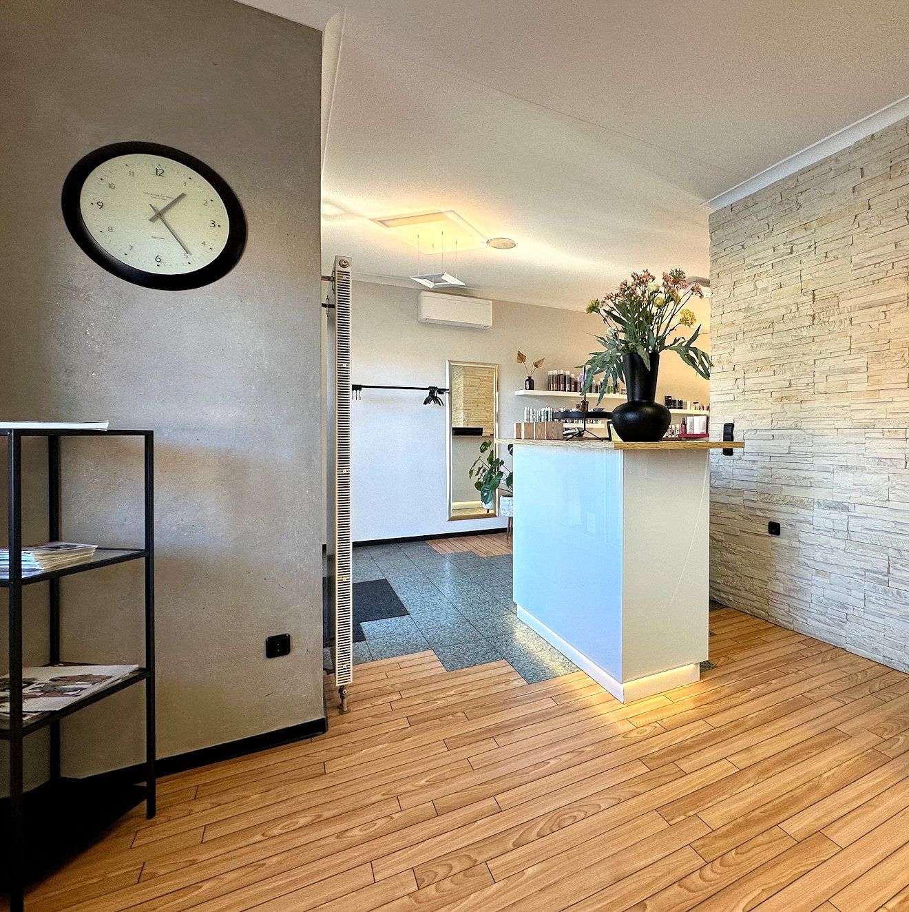 Empfangstresen des Salons mit Blumenstrauß und Naturstein-Wand